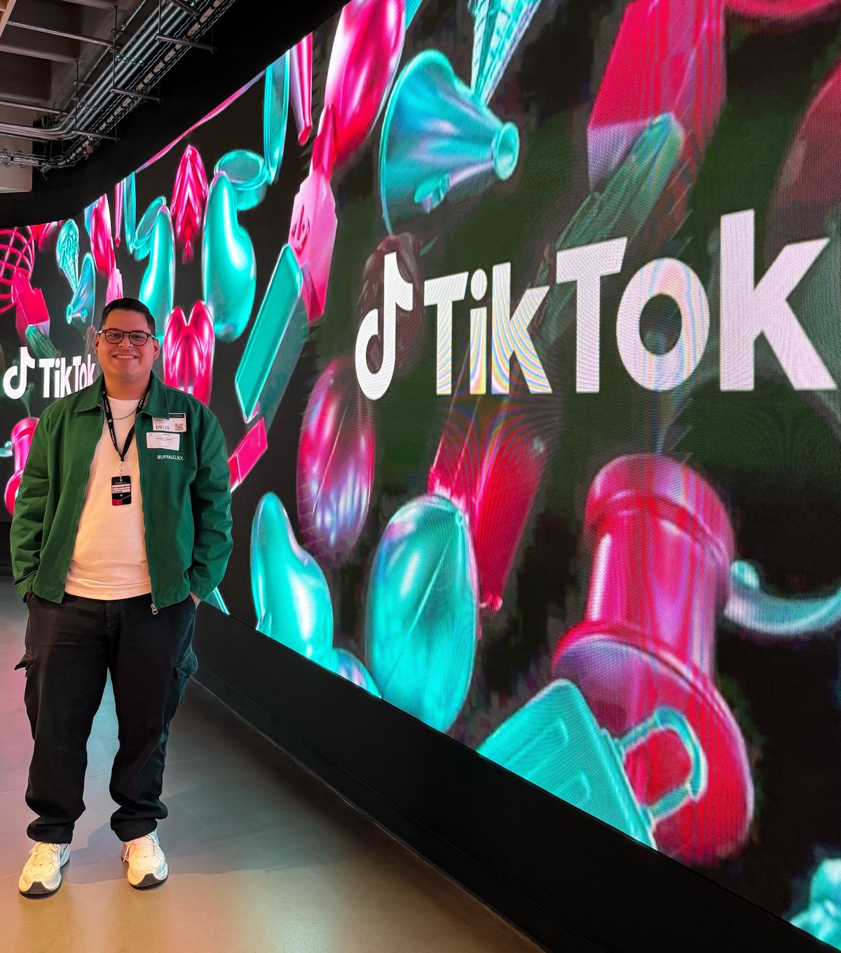 Person standing in front of a large TikTok display with neon pink and cyan graphics and the TikTok logo
