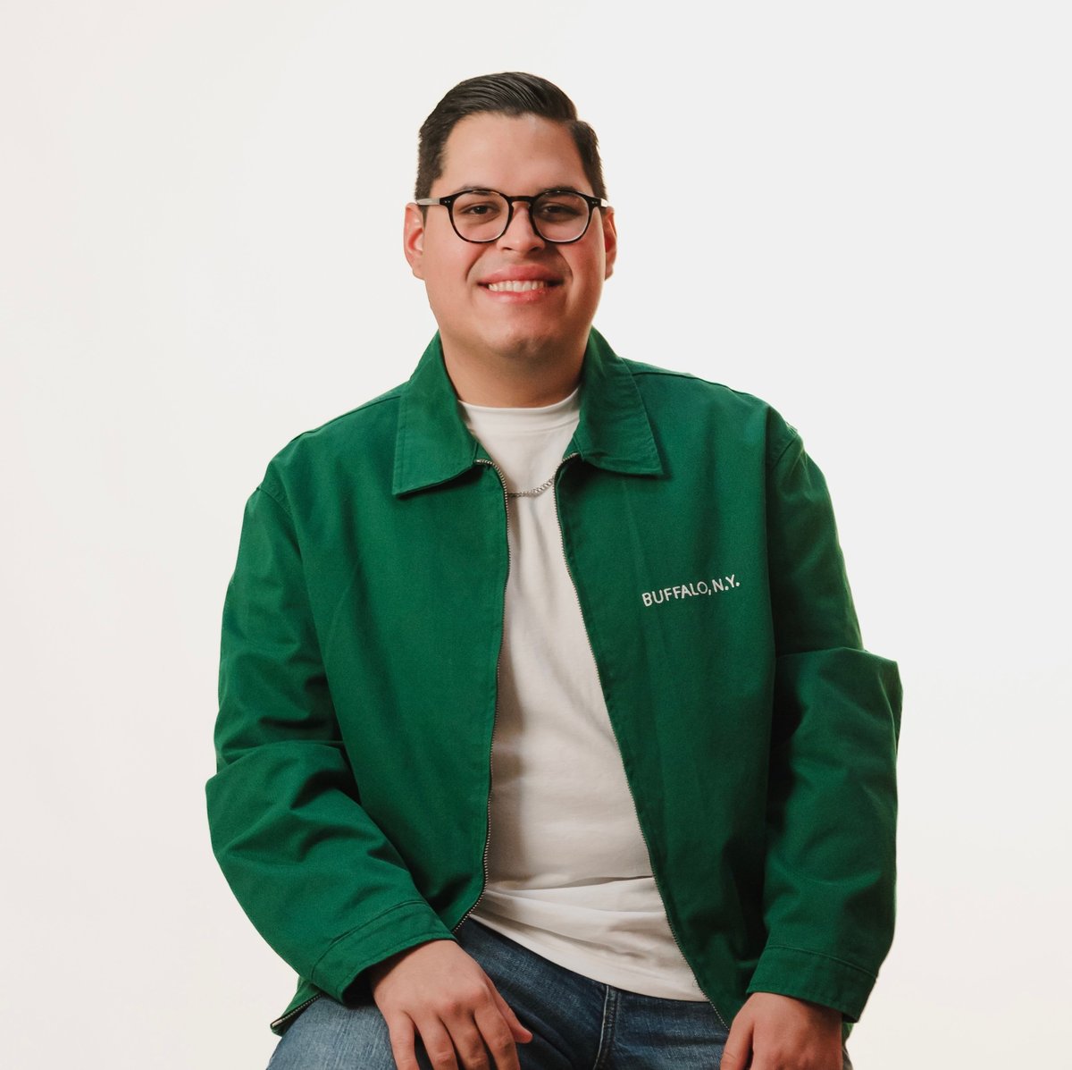 Portrait of a smiling man wearing glasses, a green jacket with company logo, and white shirt against a light gray background